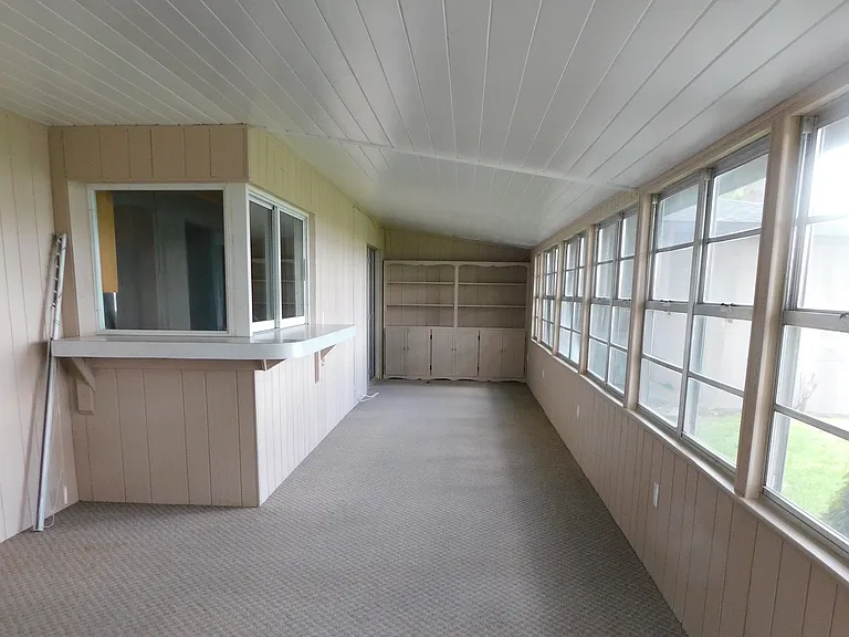 The extremely large (43.3' x 11.8') porch has a full bank of windows facing west and is carpeted with indoor-outdoor carpeting. It is not air conditioned. The windows on the left are near the kitchen sink. We're facing south.