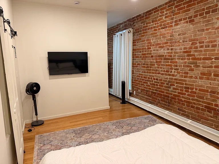 Primary bedroom with exposed brick and TV