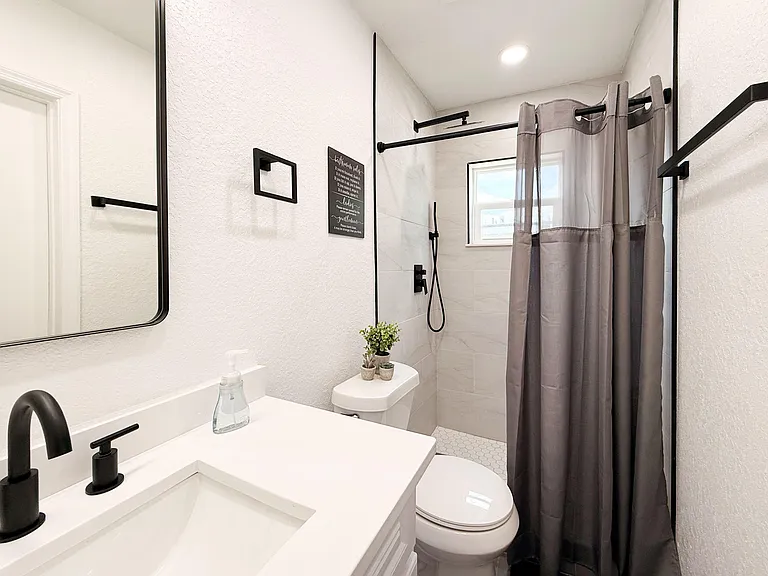 Bathroom with a vanity sink, matte-black fixtures, a tiled walk-in shower, and a window for natural light.