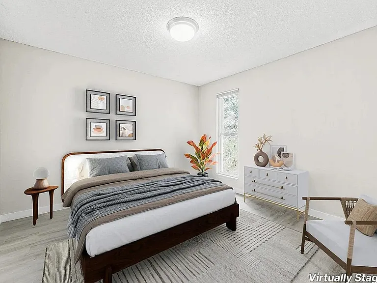 Inviting bedroom with cozy decor, featuring a comfortable bed, modern art, and a large window for natural light, virtually staged.