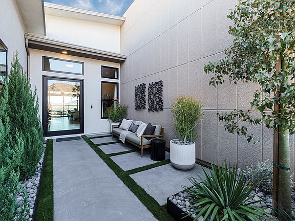 A modern and well-designed outdoor entryway with a paved walkway, lush greenery, and a cozy seating