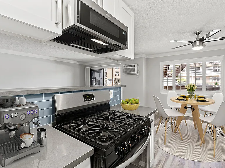Blue tiled kitchen with stainless steel oven and microwave and view of hardwood floor dining room.