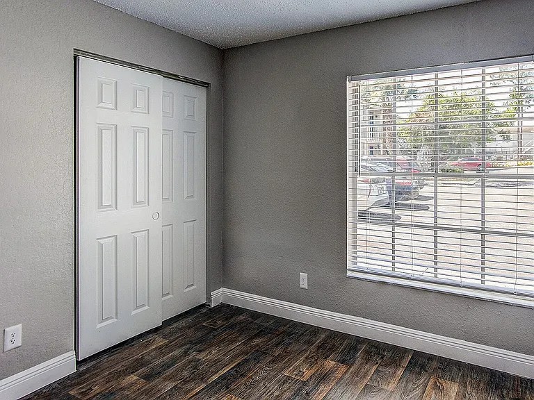 Bright and cozy room with elegant wood flooring, large window for natural light, and ample storage with a sliding door closet.