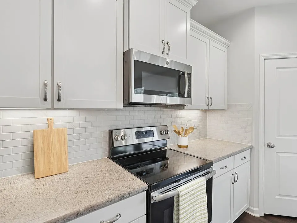 Upgrade Package kitchen with white cabinetry, designer tile backsplash, granite countertops, and stainless steel appliances