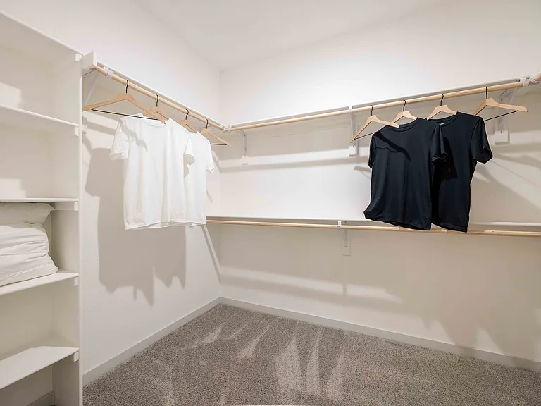 The primary walk-in closet in this Garrett Parker B1 floor plan includes double hang rods and built in shelving on two walls.