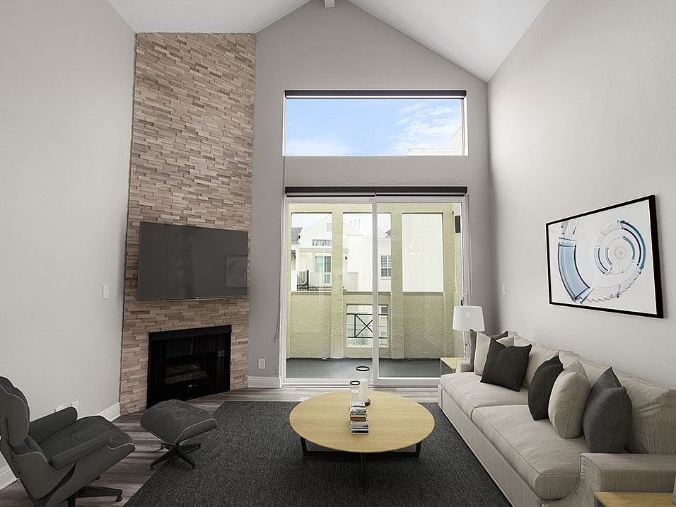 Hardwood floored living room with view of stone accent wall, fireplace, and high third-floor ceilings.