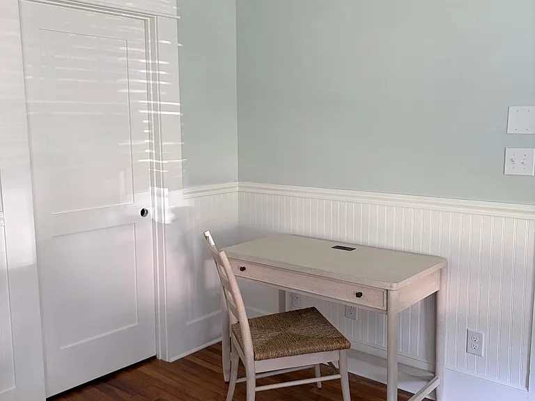 Dedicated work nook with a desk and chair, wainscoting detail, and hardwood floors near a closet for storage.