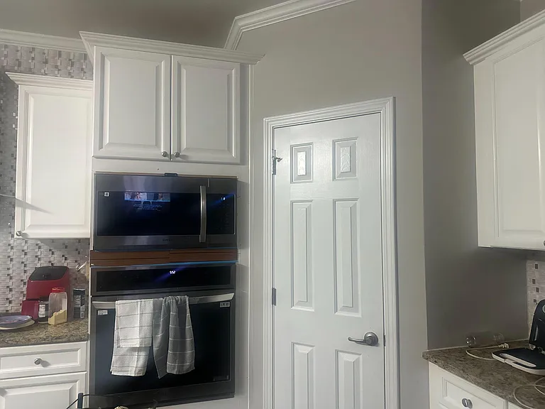Kitchen features ample white cabinetry, mosaic tile backsplash, and built-in microwave/oven for streamlined cooking.