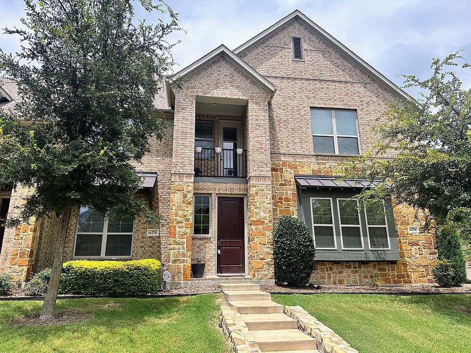 View of front facade with stone and brick siding, a front lawn, and a balcony