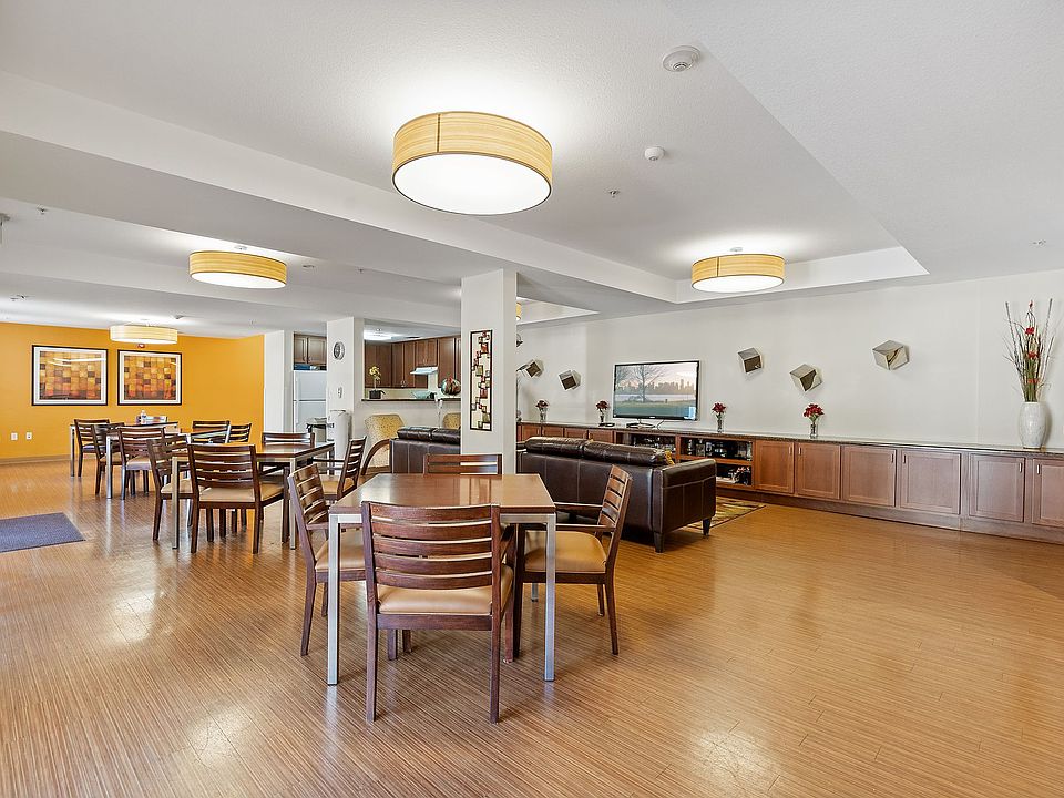 Warm and welcoming community lounge with dining tables, comfortable seating, and a TV area.