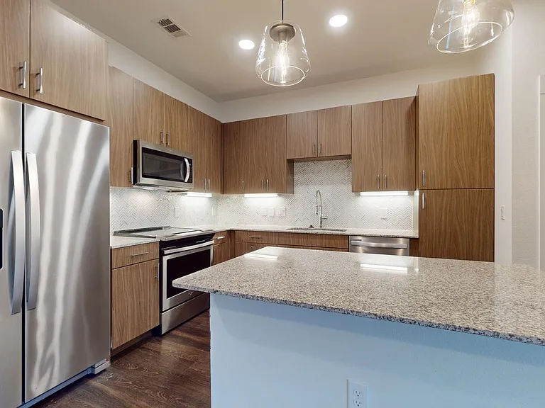 Apartment kitchen with stainless steel appliances, granite countertops, and wood-style flooring.