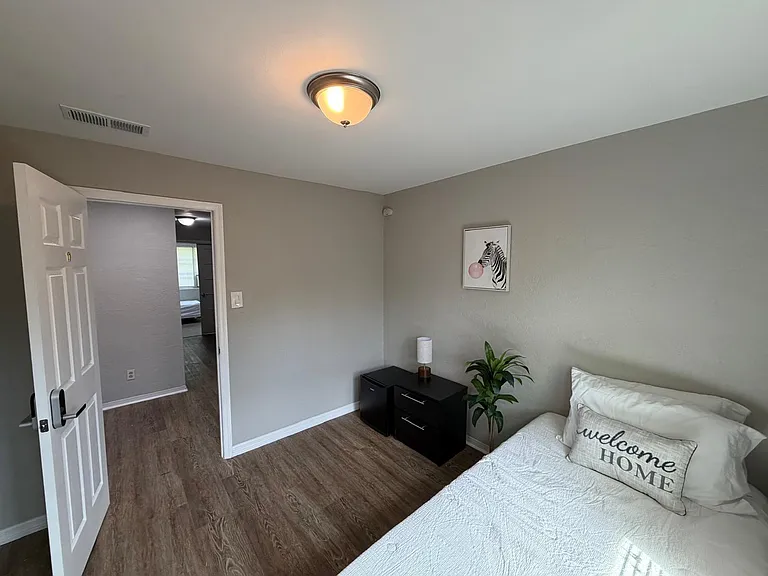 Private bedroom with wood-look flooring, neutral walls, and space for a bed plus nightstand; easy access to the hallway.