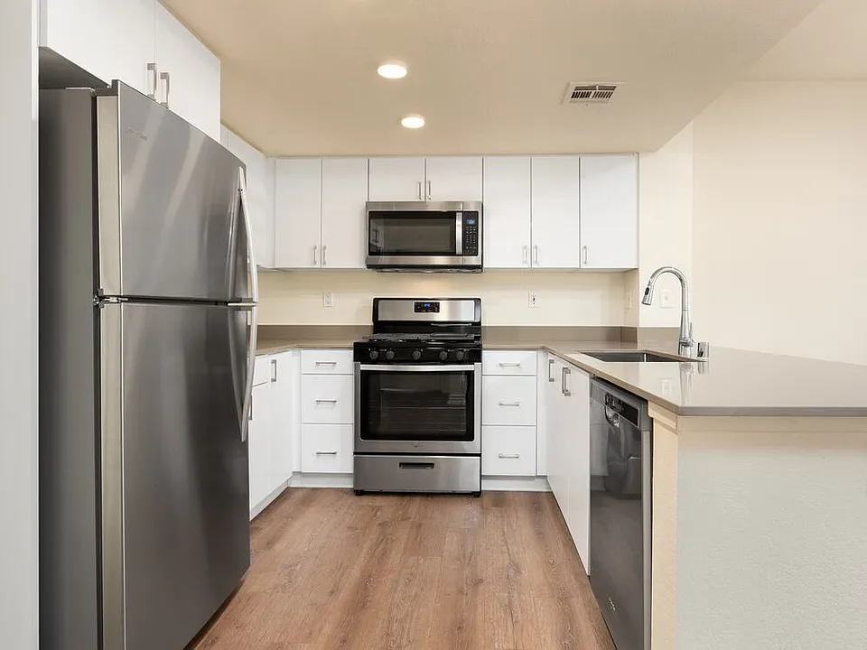 Renovated Package I kitchen with stainless steel appliances, grey quartz countertops, white flat cabinetry, and hard surface flooring