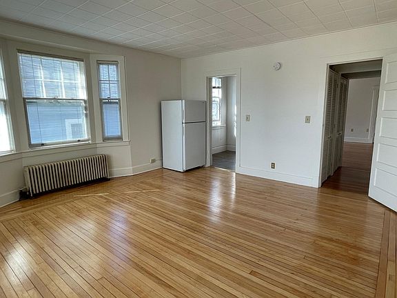 Alternate living room view showing kitchen area and hallway leading to bedroom