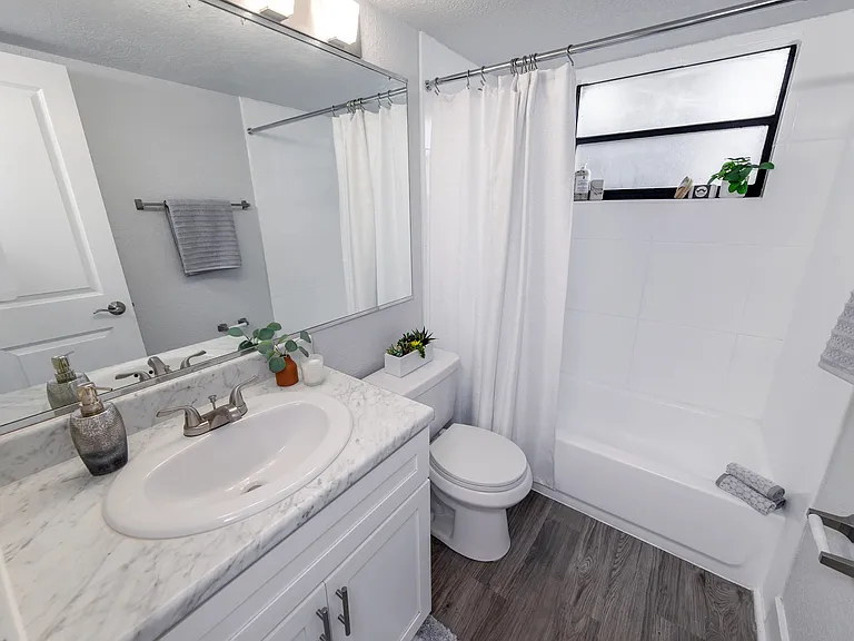 Bright and inviting bathroom featuring sleek white cabinetry, a marble vanity, and wood-style flooring.