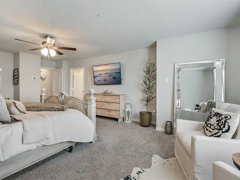 Carpeted bedroom featuring a ceiling fan, wall-mounted television, and neutral wall tones