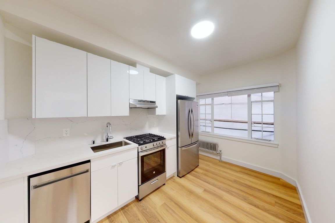kitchen featuring stainless steel appliances, cabinetry, and a window with natural light, warm wooden floors complete the look