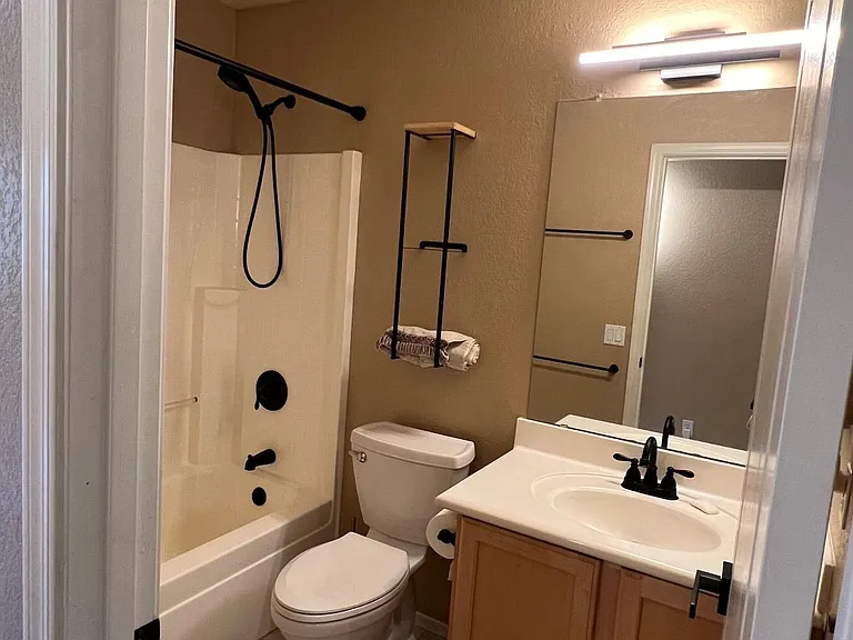 first floor full hallway bathroom with three towel racks, towel storage rack above toilet with shelf, taller toilet with elongated seat, handheld shower head for easier cleaning or washing pets in tub or cannot fit in garage laundry sink
