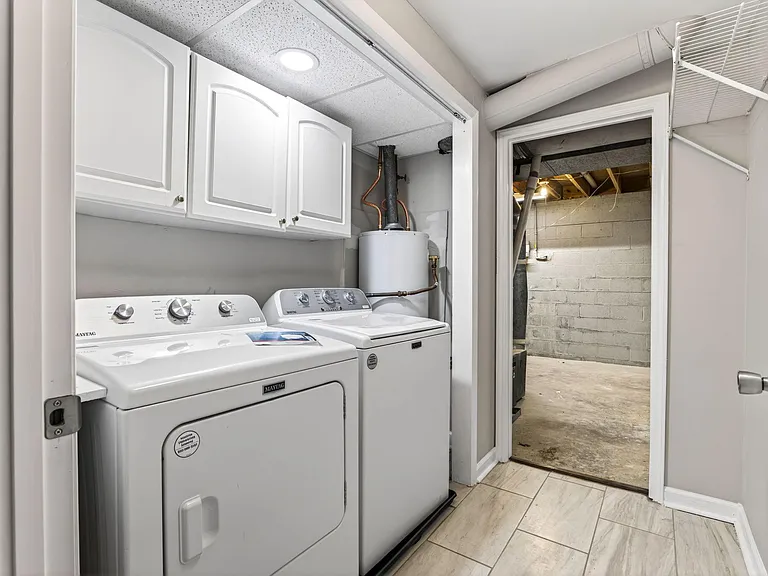 Dedicated laundry area with side-by-side washer/dryer, overhead cabinetry, and easy access to utility/storage space.