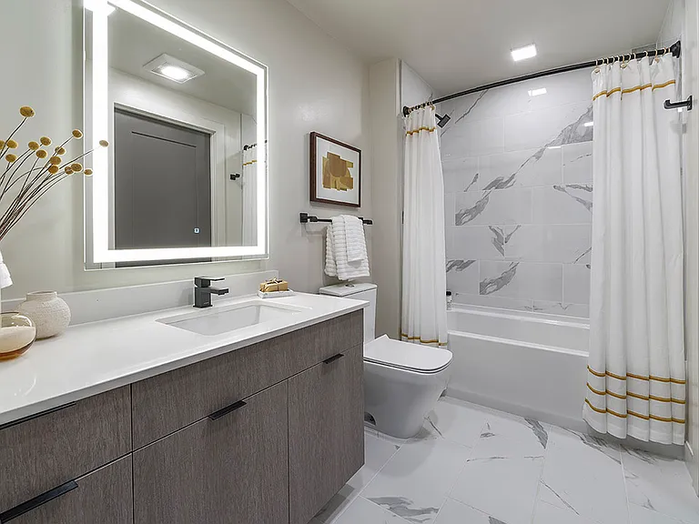 Apartment bathroom with large soaking tub, tile flooring, and LED vanity mirror.