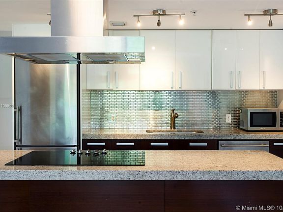 Kitchen with large cooking island, stainless appliances, and modern glass tile backsplash. 
