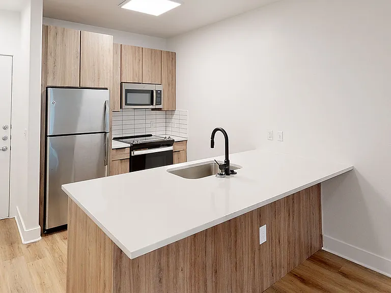 Apartment kitchen with stainless steel appliances, quartz countertops and wood-style flooring.