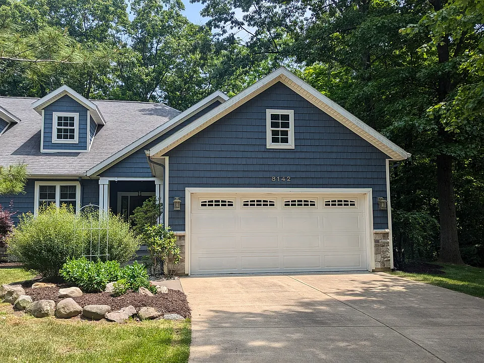 Outside entry with nautical blue exterior, beautiful landscaping, concrete driveway and attached two-car garage.