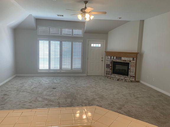 Large living room with electric fireplace, ceiling fan and large windows with wood shutters. Los of light.