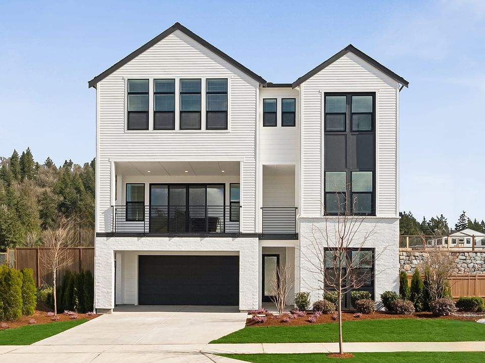 A modern, two-story house with a garage, surrounded by a well-manicured lawn and trees in the backgr