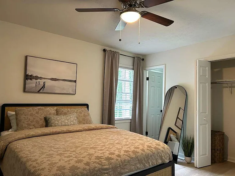 Furnished bedroom with a queen bed, ceiling fan, window with curtains, and an open closet for convenient storage.