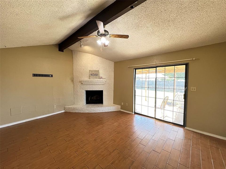 Unfurnished living room with brick wall, a fireplace, ceiling fan, hardwood / wood-style flooring, and lofted ceiling with beams
