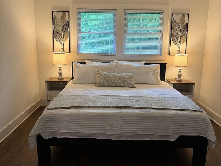 Furnished bedroom featuring a queen bed, matching nightstands, ceiling fan, and dual windows with blinds.