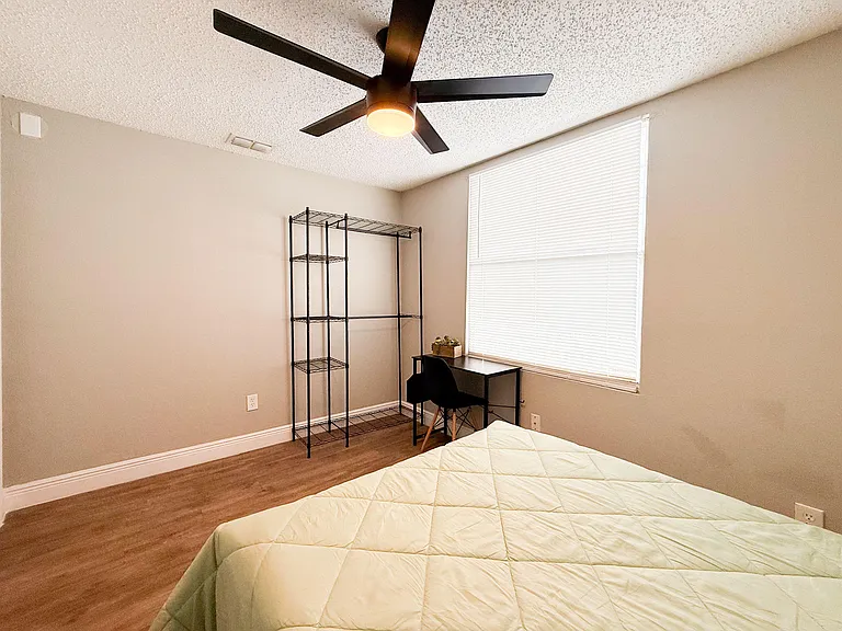 Bedroom offers a ceiling fan with light, a large window with blinds, and space for a desk plus open shelving storage.