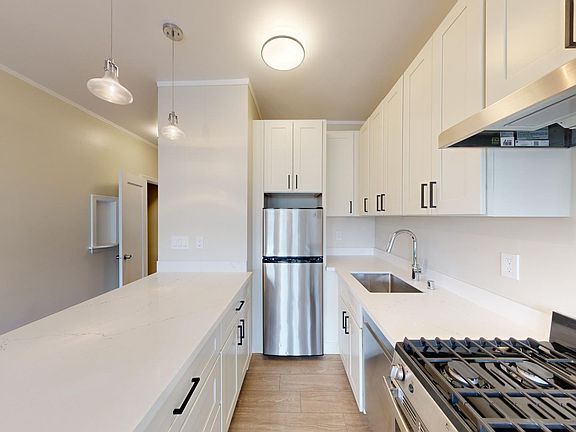 Kitchen with multiple cabinets, refrigerator, stove, range hood, and sink