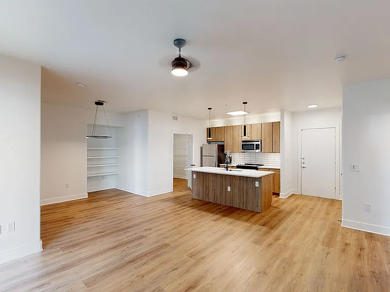 Apartment kitchen with stainless steel appliances, dining and living room with wood-style flooring.