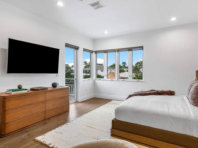 Bright and airy bedroom with sleek wooden furnishings, soft rugs, and serene views from large windows.