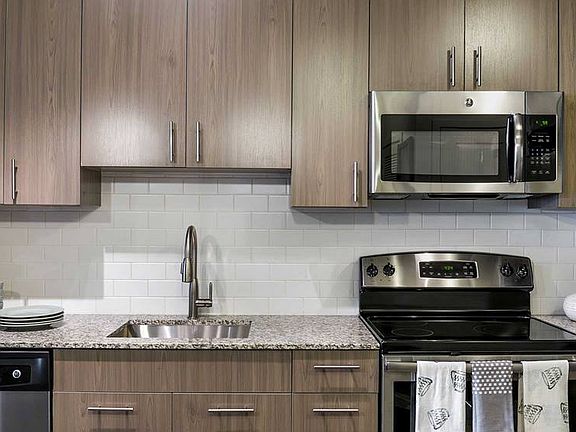Kitchen with brown cabinetry, granite countertops with tile backsplash and stainless steel appliances