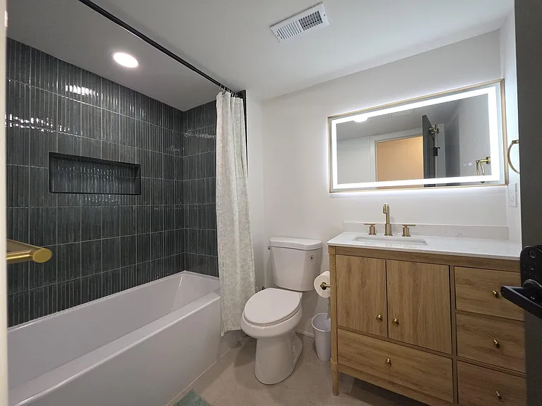 Updated full bath with tub/shower surround, tiled walls, and a spacious vanity topped with an illuminated mirror.