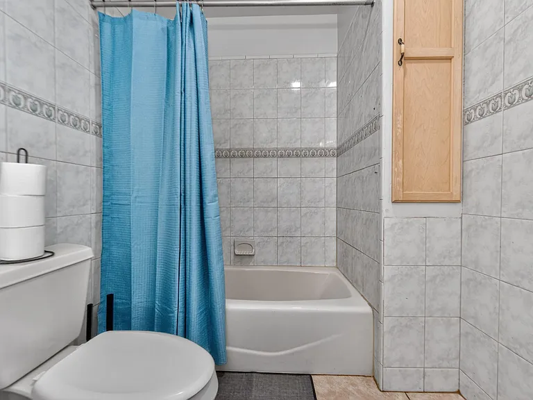 Full bathroom with tiled tub/shower surround, shower curtain, and wall-mounted storage cabinet for toiletries.