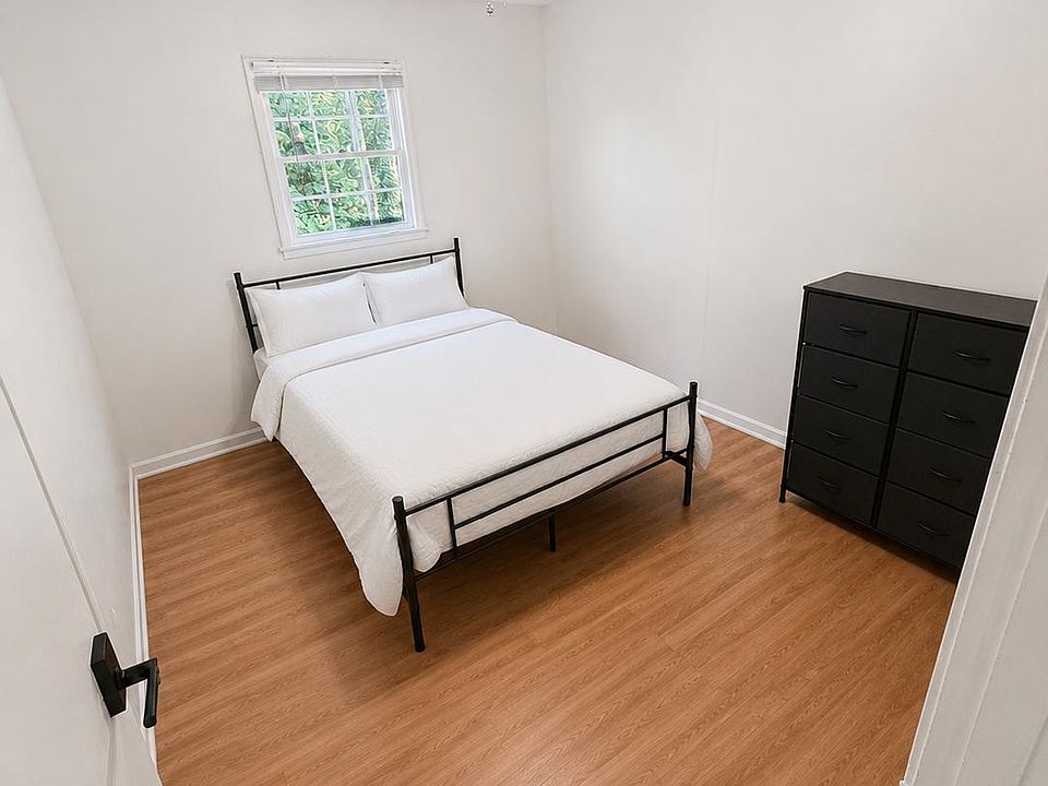 Furnished bedroom with a full bed, dresser storage, wood-look flooring, and a window with leafy outdoor views.