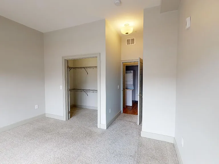 Spacious apartment bedroom with large closet and plush carpet flooring.