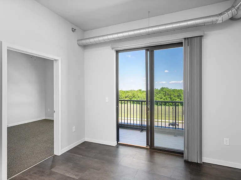 Bright apartment interior with large sliding glass doors opening to a balcony with a scenic view, featuring modern gray flooring and an inviting open space. Bright apartment interior with large sliding glass doors opening to a balcony with a scenic view,