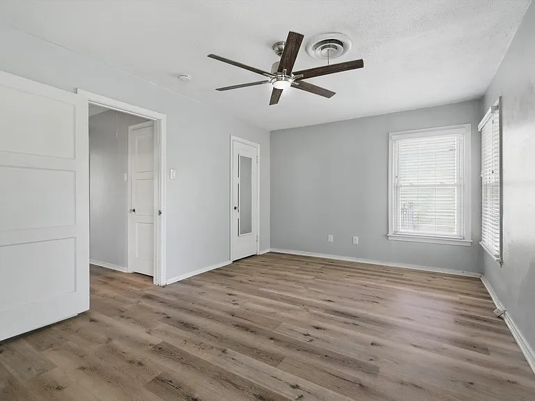 Large primary bedroom featuring neutral soft grey paint, LVP flooring, ceiling fan, closet and multiple windows providing beautiful natural light.