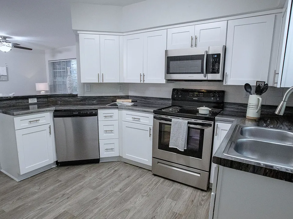 The black fusion countertops, white shaker cabinetry, and stainless-steel appliances add a touch of elegance to your kitchen, surrounded by ample cabinet space for all your culinary essentials.
