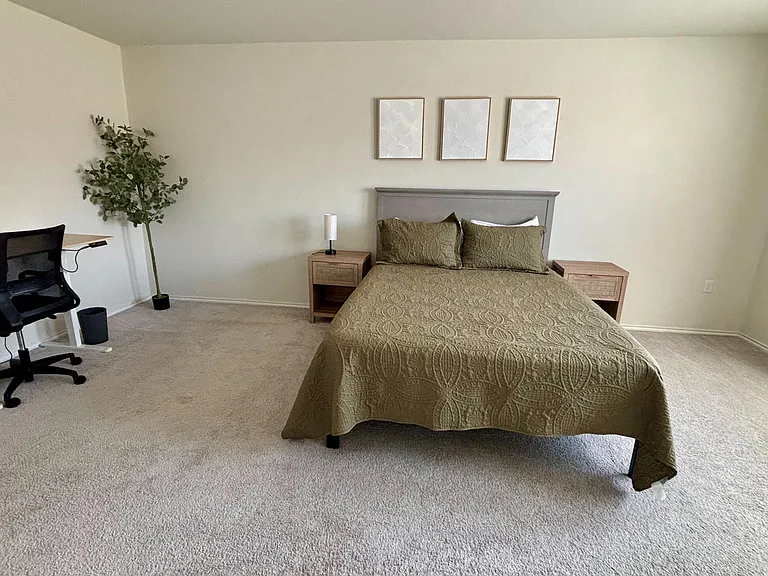 Spacious furnished bedroom with a full bed, matching nightstands, and a dedicated desk area with chair.