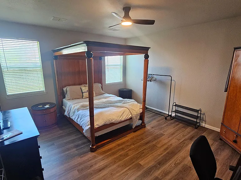 Furnished bedroom with a four-poster bed, two windows, ceiling fan, and ample storage including an armoire and dresser.