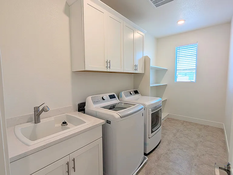 This well-planned, independent laundry room features abundant natural light. Equipped with a practical utility sink, ample cabinetry, and open shelving, this spacious area makes organization effortless_a must-have space for modern daily living.