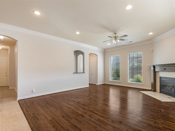 Spacious living area featuring wood-finish flooring, a decorative fireplace with mantel, recessed lighting, and crown molding