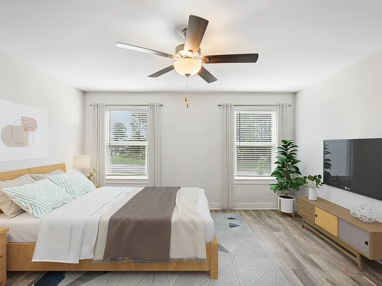 Another perspective view of the serene primary suite, showcasing a modern ceiling fan, sleek entertainment, and sunlit window views.