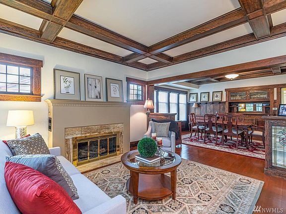Great room offers original wood floors, 9 ft box beam ceiling, leaded glass bookcases and woodburning fireplace with fan